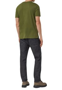 Olijfgroene katoenen T-shirt gecombineerd met donkergrijze spijkerbroek, voorzien van een standaard ronde hals en korte mouwen. Schoeisel is lichtbruin met een stevige zool.