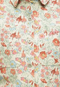 Υφάσμα με λουλουδάτο μοτίβο σε κόκκινα, ροζ, μπλε και κίτρινα λουλούδια πάνω σε ανοιχτό μπεζ φόντο και τέσσερα ασημένια κουμπιά με τρουκ στη μέση.