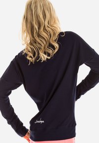 Granatowa bluza z długim rękawem o luźnym kroju, z okrągłym dekoltem i haftowanym detalem "Jinshape" przy dolnej krawędzi. Gładka tekstura materiału.