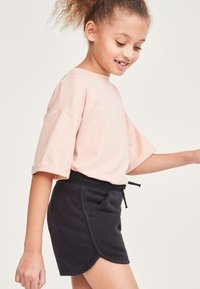 Helle rosa Baumwoll-T-Shirt mit großen Ärmeln, kombiniert mit einem schwarzen, elastischen Jerseykleid mit strukturiertem Material und abgerundetem Saum.