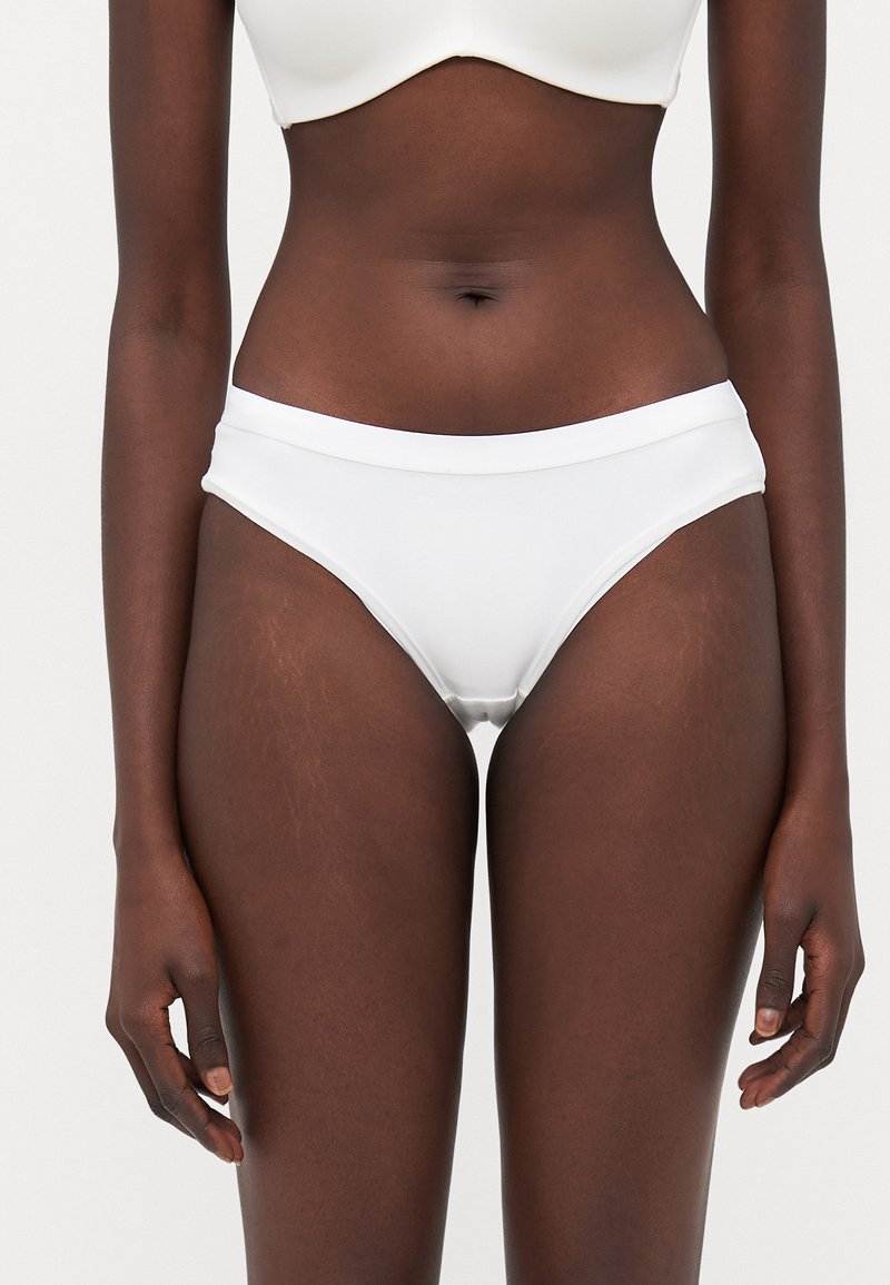 Białe majtki bikini wykonane z gładkiego, elastycznego materiału. Charakteryzują się niskim stanem z szerokim pasem w talii i minimalnym zakryciem.