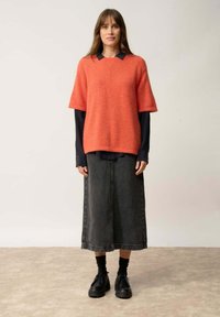 Suéter de punto coral de manga corta sobre una camisa oscura con cuello, combinado con una falda larga de mezclilla oscura y zapatos negros con cordones.
