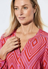 Rode en roze blouse met patroon, met een v-hals, featuring geometrische vormen, knoopsluiting en een subtiele textuur op de mouwen.