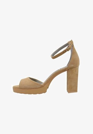 Sandale à talons hauts en suede beige avec un bout ouvert, une sangle au niveau de la cheville et un talon épais. La semelle plateforme ajoute de la hauteur et de la stabilité. Semelle extérieure en caoutchouc texturé.