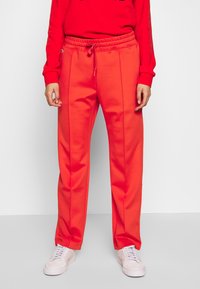 Rode sweatpants met een trekkoord in de taille, een gladde textuur en zijnaaddetails, gecombineerd met witte sneakers en een bijpassend rood top.
