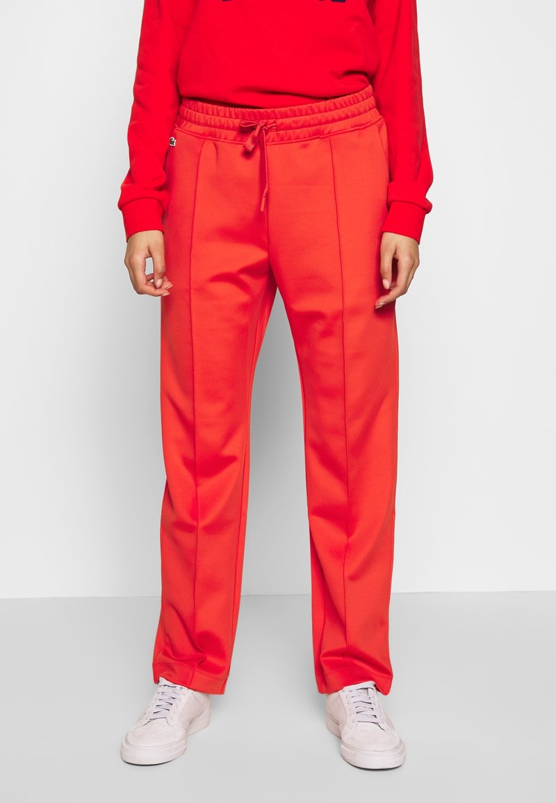 Rode sweatpants met een trekkoord in de taille, een gladde textuur en zijnaaddetails, gecombineerd met witte sneakers en een bijpassend rood top.