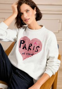 Svetlošedý mikina s veľkým srdcom s červenými a bielymi pruhmi. Na ňom je text "PARÍŽ" čiernou farbou a pod ním "je t'aime".