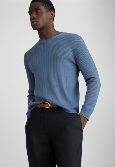 Maglione blu a coste con scollatura a V e maniche lunghe, abbinato a pantaloni scuri e una cintura marrone con una fibbia circolare dorata.