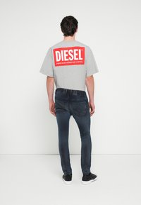 Hall halli lühikeste varrukatega T-särk, millel on seljal suur punane "DIESEL" logo, kombineeritud tumelate siniste kitsaste teksapükstega ja mustade tossudega.