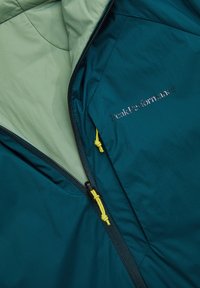 Turquoise jas met lichtgroene voering, zwarte ritssluiting met gele trekkoorden en het "Peak Performance"-logo geborduurd op de borst.