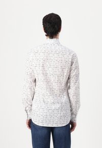Knappe skjorte i hvit med svart håndskrevet tekstmønster. Har lange ermer og rundet kant. Stoffet har en glatt tekstur.