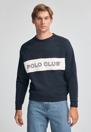 Sudadera navy con una banda horizontal crema que presenta el texto "POLO CLUB". Puños y dobladillo acanalados, diseño clásico de cuello redondo.