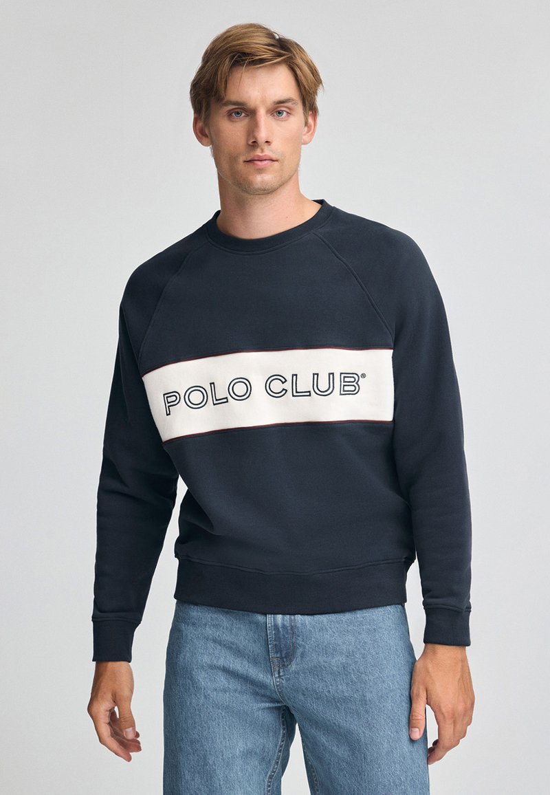 Sudadera navy con una banda horizontal crema que presenta el texto "POLO CLUB". Puños y dobladillo acanalados, diseño clásico de cuello redondo.