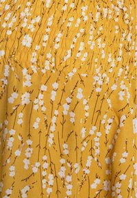 Tissu de robe florale jaune avec des fleurs blanches et roses, tiges brunes ; présente une texture froncée dans la partie supérieure, texture lisse dans l'ensemble.