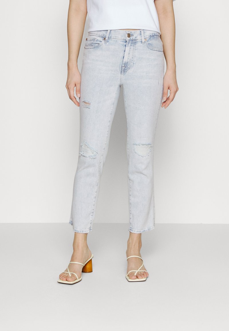 Jeans rupta de culoare albastru deschis, cu talie înaltă și design drept, având petice distresate și margini desfăcute. Purtați cu sandale cu toc bej.