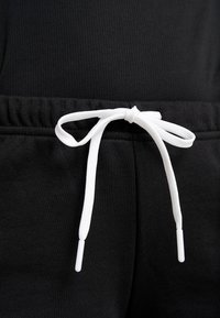 Pantalones de chándal negros con una tela texturizada, cinturilla elástica y cordón blanco con puntas de plástico. Vista detallada del área de la cinturilla.
