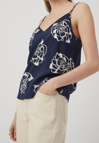 Námořnická modrá bezrukávová blůza s V-výstřihem a bílým květinovým vzorem, s tenkými ramínky a volným střihem.