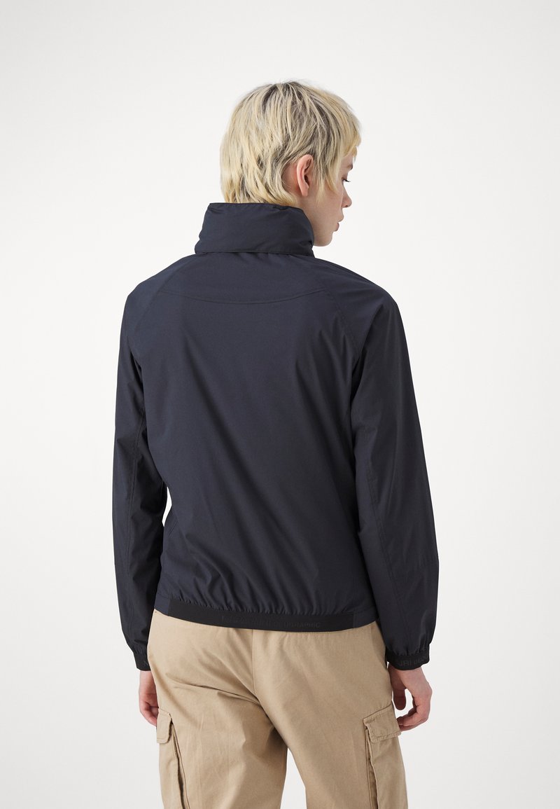 Giacca a vento blu navy con colletto alto e polsini elastici. Texture liscia e silhouette aderente, che termina all'altezza della vita con un orlo elastico.