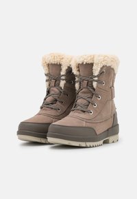 Een paar beige winterlaarzen met een voering van bont, vetersluiting aan de voorkant en rubberen zolen, tegen een effen witte achtergrond.