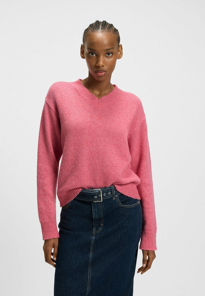 Rosa Wollmischung Pullover mit V-Ausschnitt, langen Ärmeln, gerippten Bündchen und Saum. Kombiniert mit einem dunklen Jeansrock für einen lässigen Look.