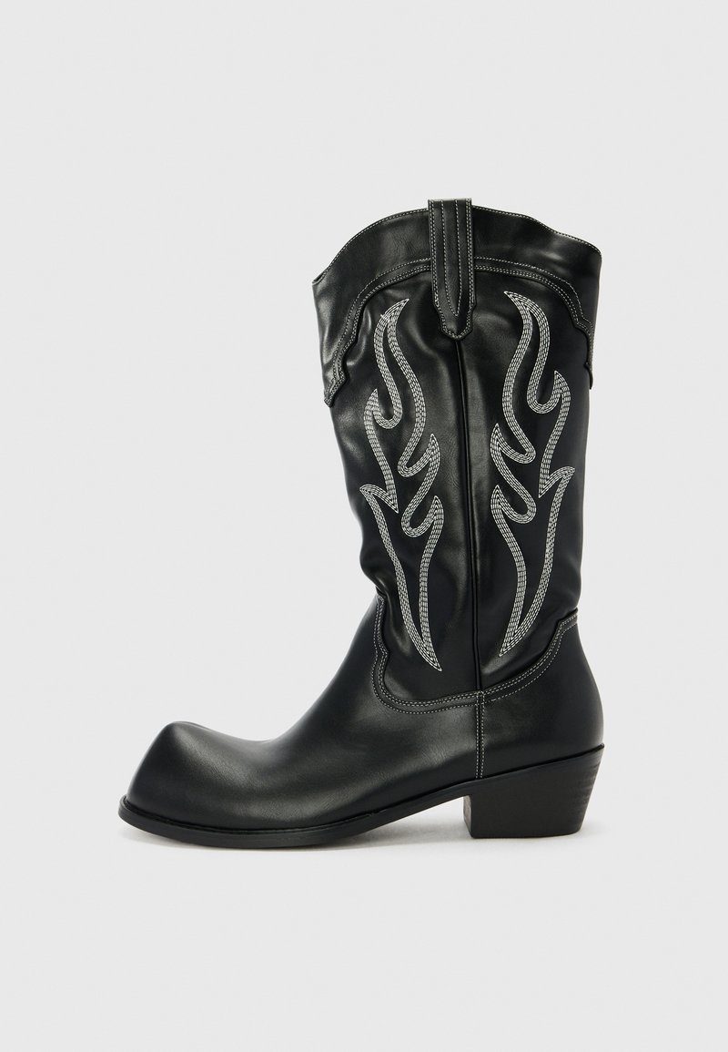 Botas de vaquero de cuero negro con bordado de llamas metálicas plateadas, punta afilada y un tacón bajo apilado. Textura suave y borde superior redondeado.