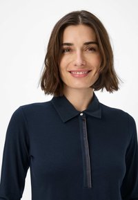 Marineblå langærmet polo-shirt med knapkrave og lynlåsdetalje, lavet af glat stof med en tætsiddende form og minimalistisk design.