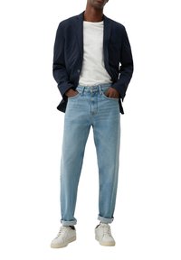 Marineblazer, weißes Rundhals-T-Shirt, hellblaue Denim-Jeans und weiße Sneaker. Die Jeans haben eine lockere Passform mit umgeschlagenen Säumen.