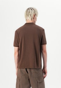 Brown short-sleeve polo shirt made of cotton, featuring a classic collar, visible stitching, and a relaxed fit.