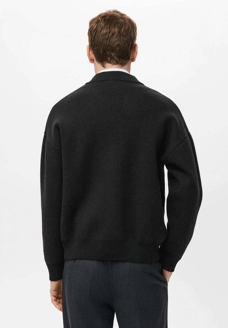Zwarte gebreide trui met een relaxte pasvorm, geribbelde manchetten en zoom. De textuur lijkt dik en zacht met een klassieke ronde hals.