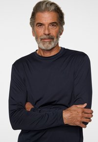 Marinblå långärmad skjorta i mjukt, stretchigt material. Har en rund halsringning och en subtil logotypdesign på bröstet. Slät textur.