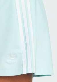 Light blue athletic skirt with white three-stripe design and embroidered logo. Features a smooth, stretchy fabric and a straight hemline.