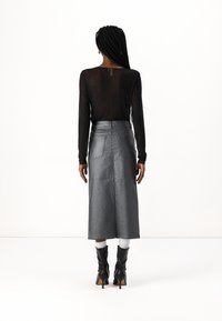Haut noir à manches longues avec une texture transparente et des embellissements, associé à une jupe midi en denim argentée taille haute et des bottes noires à talons.