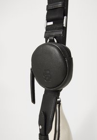 Black circular pouch with textured leather, attached to a sturdy strap featuring metal hardware; tan body with black and white stripe accents.