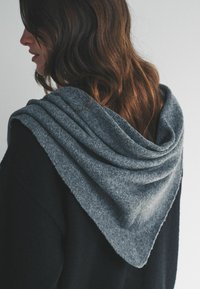 Grå sjal lavet af blødt, tekstureret stof lagt over et sort plagg, der har et trekantet design og lagdelte folder bagpå.