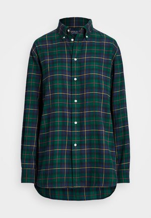 Chemise à carreaux verte, bleu marine et jaune, à manches longues avec col boutonné et boutons blancs, présentée sur un fond blanc.