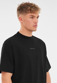 Černé oversize tričko vyrobené z bavlny, s krátkými rukávy a kulatým výstřihem. Obsahuje decentní logo "Johnny Urban" na hrudi.