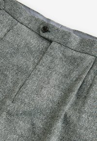 Grau gemustertes Gewebe mit einem Fischgrätmuster, das einen flachen Bund und einen Knopfverschluss aufweist, eine glatte Textur und einen dezenter Glanz hat.