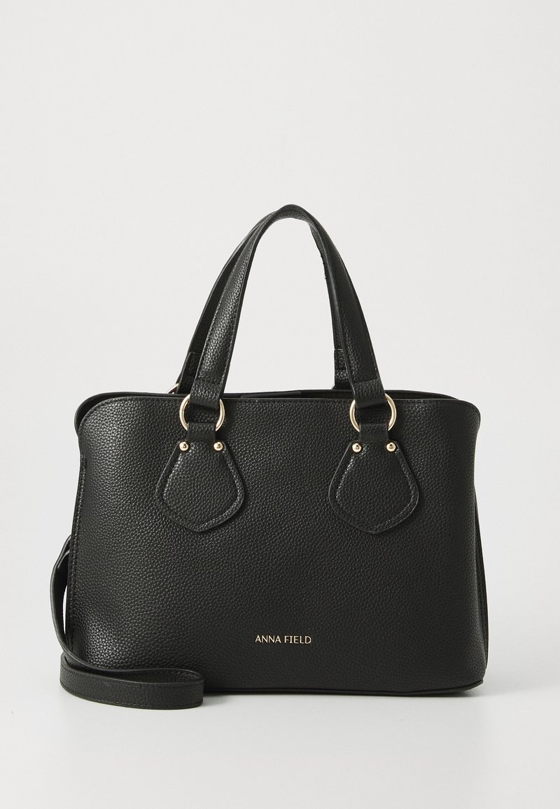 Sac à main en cuir noir texturé avec double poignée, bandoulière amovible, quincaillerie dorée et logo "ANNA FIELD" au centre devant.