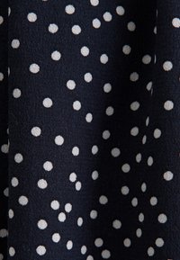 Tessuto blu navy con pois bianchi; una trama texturizzata crea profondità e interesse visivo. Pois distribuiti uniformemente attraverso il materiale.