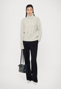 Pull en maille épaisse à col roulé gris clair, associé à un pantalon rayé bleu marine. Complété par un sac à main noir avec une ceinture en accent.