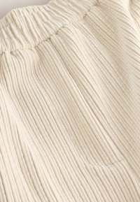 Tejido de pana beige con textura ribeteada vertical, que presenta una cinturilla fruncida y un acabado suave, mostrando un material suave y aterciopelado.