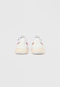 Sneaker bianca con dettagli rossi, texture in pelle liscia, forma arrotondata e suola ammortizzata. Dotata di linguette sul tallone per una facile calzata.