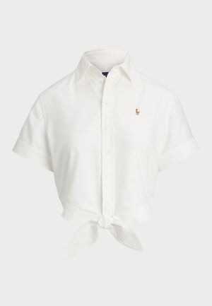 Camisa blanca de manga corta hecha de algodón, con un dobladillo atado, cuello puntiagudo y pequeño logo bordado en el lado izquierdo del pecho.