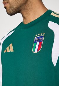 Grøn fodboldtrøje med hvide sideaccenter, gyldt Adidas-logo og Italiens landsholdsvåben med blå, rød og hvid detaljering.