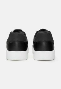 Une paire de baskets basses noires avec des semelles blanches, présentées de l'arrière sur un fond clair.
