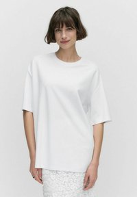 Vit oversized t-shirt i mjukt material med korta ärmar och rund halsringning, tillsammans med en texturerad vit spetskjol.