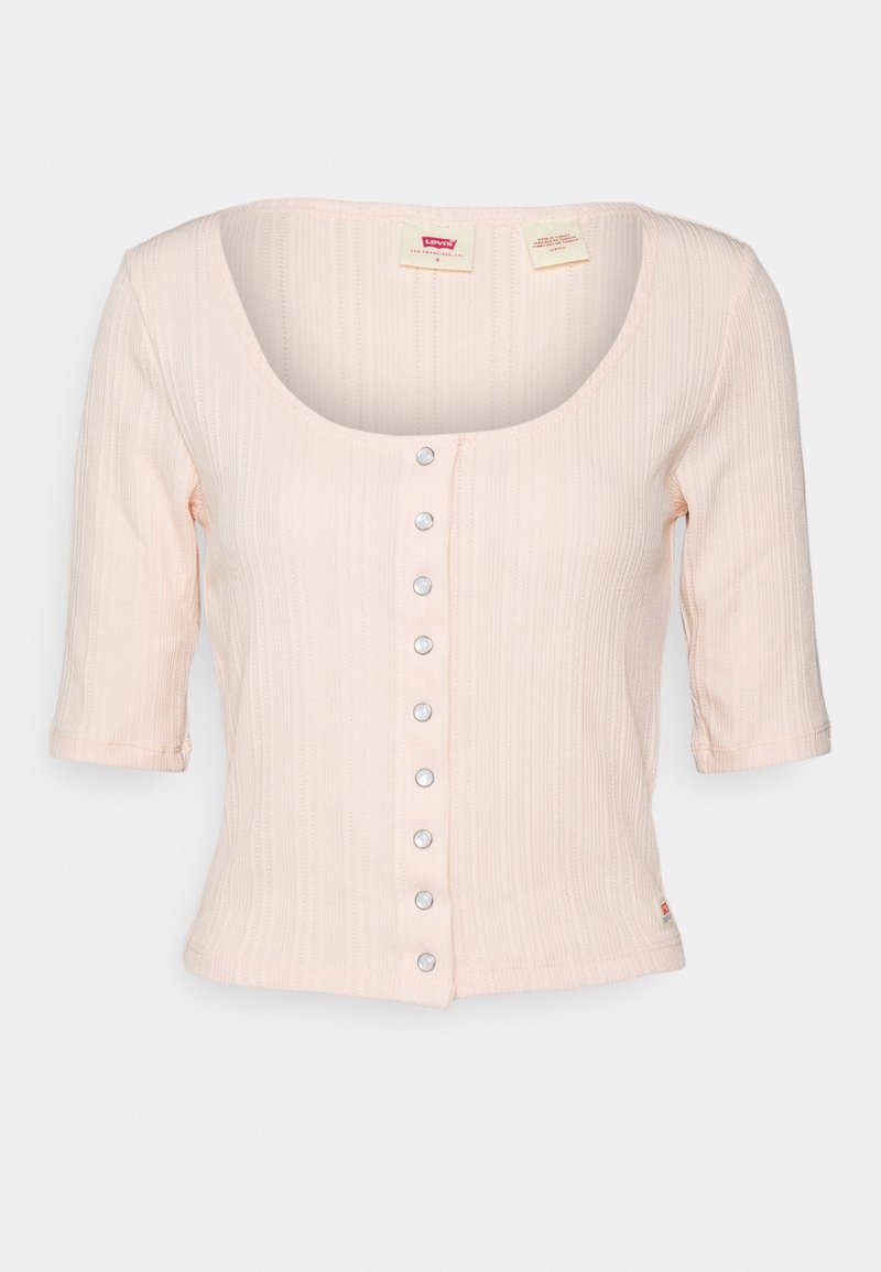 Haut côtelé rose clair avec une encolure dégagée, des manches trois-quarts et une rangée de boutons en argent sur le devant. Texture douce, coupe décontractée.