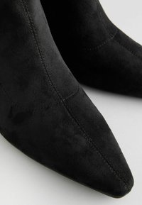 Schwarze Wildleder-Stiefeletten mit spitzem Toe, glatter Textur und dezenten Steppdetails an den Seiten.