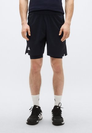 Shorts de sport noirs en tissu léger, avec une ceinture élastique, des fentes latérales et un petit logo blanc sur la jambe gauche.