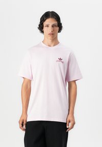 Hellrosa Baumwoll-T-Shirt mit kurzen Ärmeln, geripptem Rundhalsausschnitt und kleinem dunkelrotem Adidas-Logo auf der linken Brust.